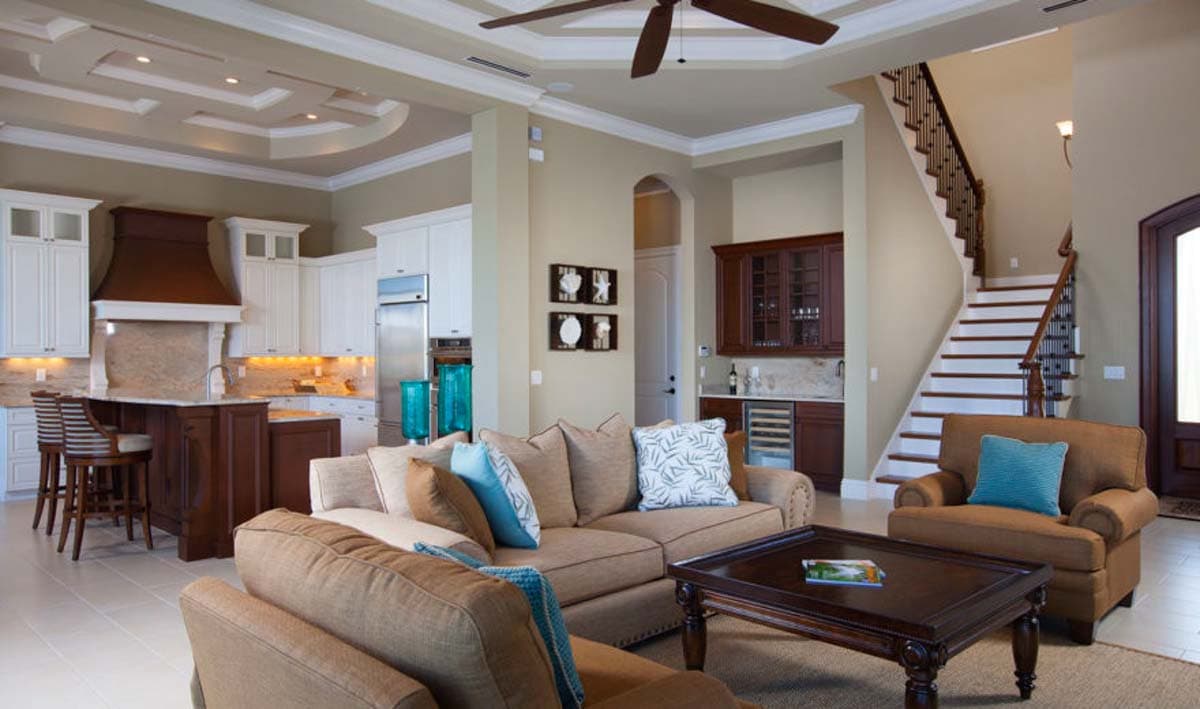 Interior view of open-concept living area with coffered ceiling, kitchen island, wet bar, and staircase.