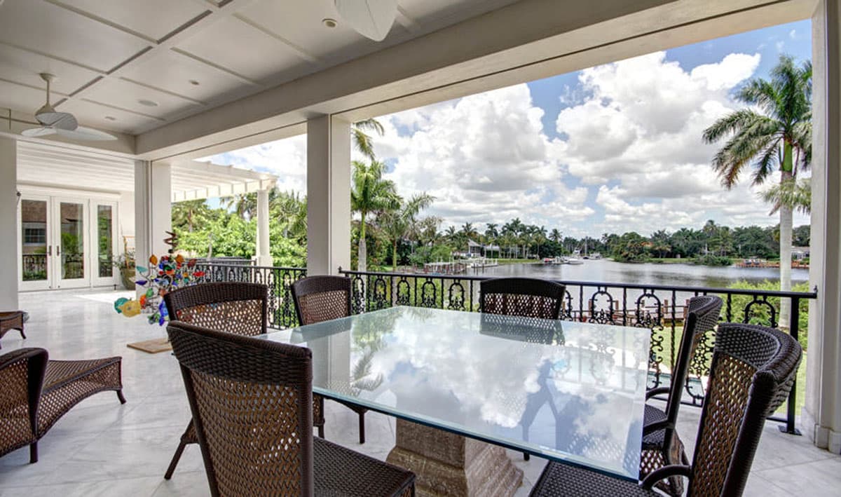 Covered patio with outdoor dining furniture and a water view, featuring French doors and a coffered ceiling.