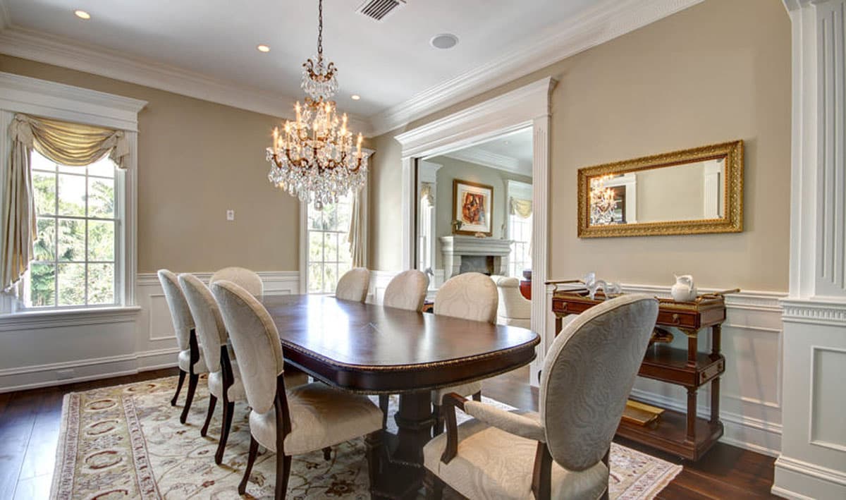 Formal dining room with large wood table, upholstered chairs, chandelier, and ornate mirror.