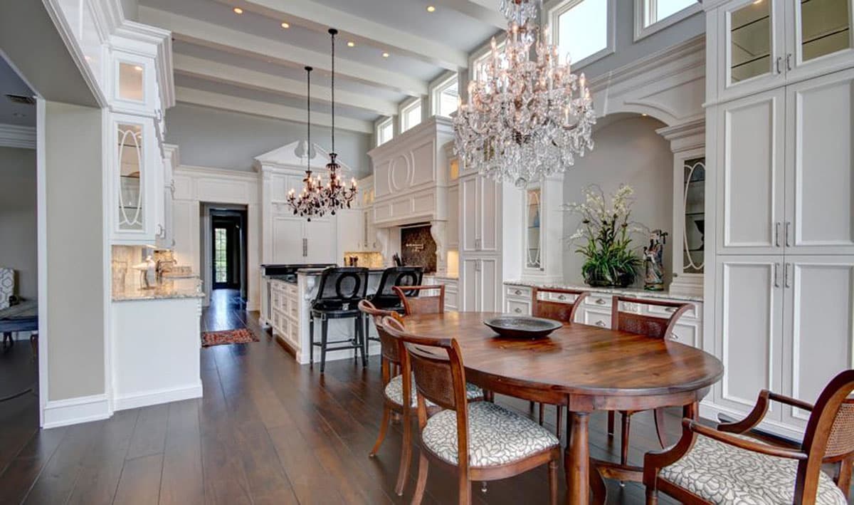 Interior view of a spacious kitchen and dining area with a large island, vaulted beamed ceiling, and crystal chandeliers.