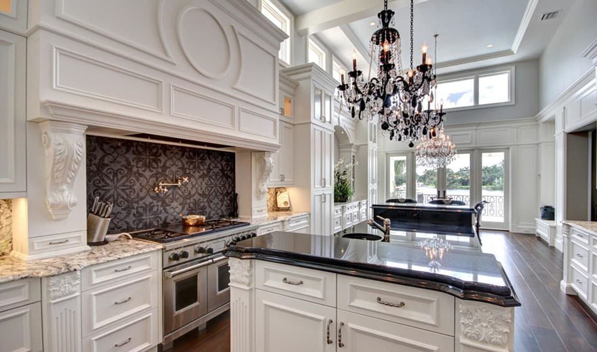 Kitchen with large island, ornate range hood with decorative tile backsplash, and crystal chandeliers.