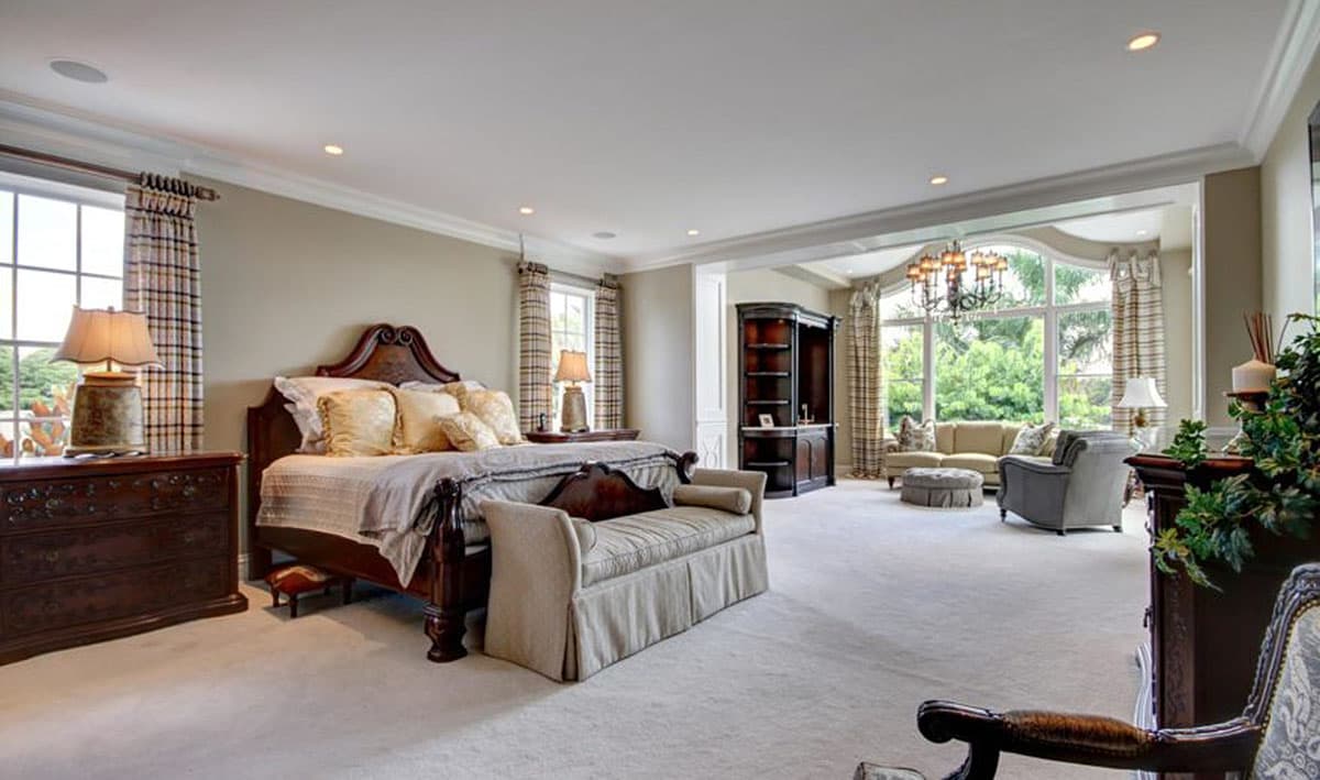 Primary bedroom with large bed, dresser, bench, and seating area with chandelier and large windows.