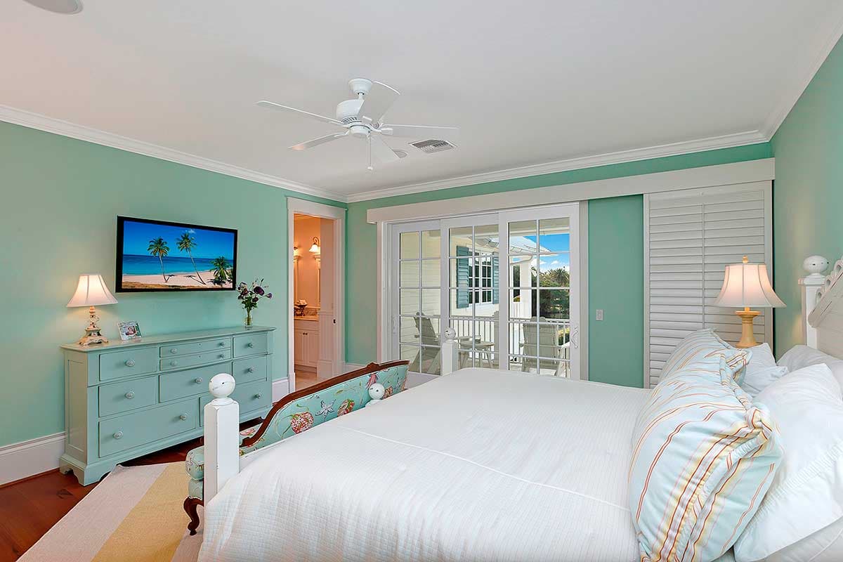 Bedroom with seafoam green walls, a dresser, large sliding glass doors to a porch, and a ceiling fan.