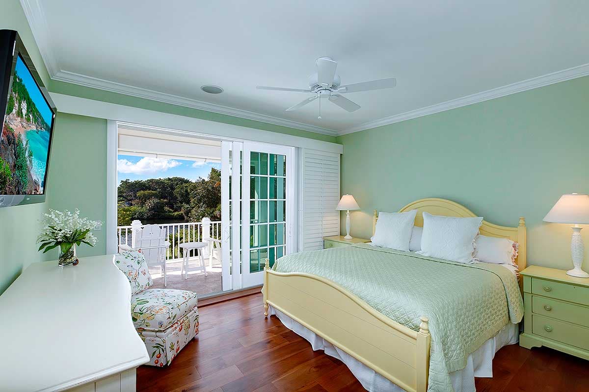 Bedroom interior with queen bed, dresser, chair, and sliding glass doors opening to a balcony.