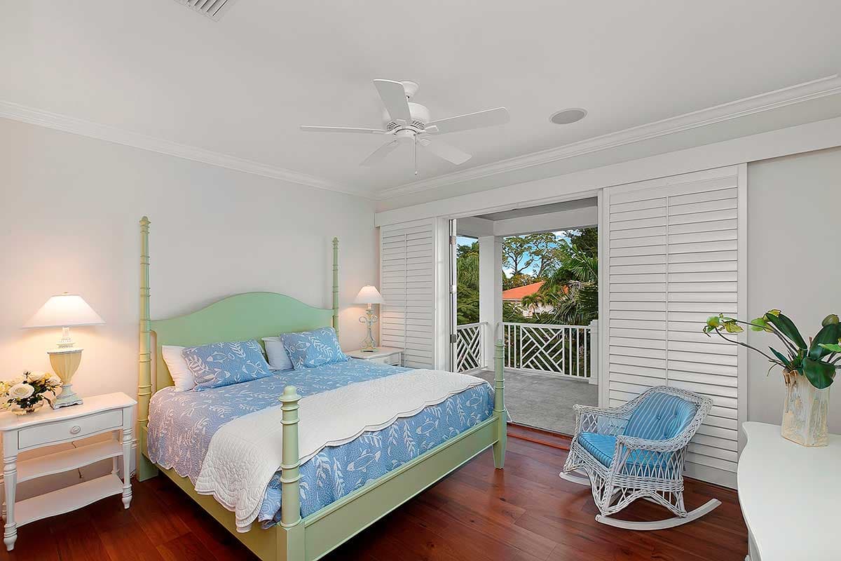 Bedroom with canopy bed, white louvered shutters, and access to a covered porch with decorative railing.