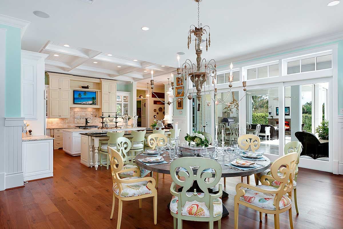 Interior view of a dining room and kitchen with a coffered ceiling, island, and large sliding glass doors.
