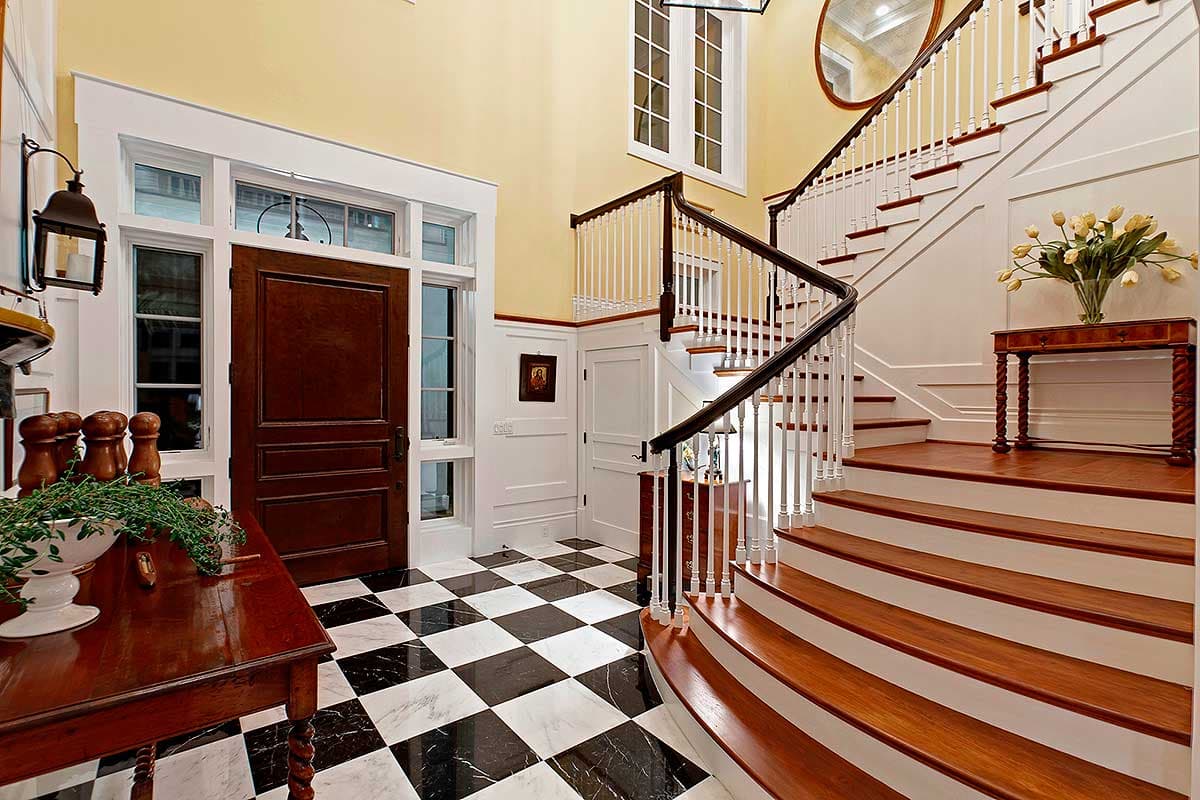 Grand foyer with paneled wainscoting, checkered marble floor, and curved staircase with white balusters.
