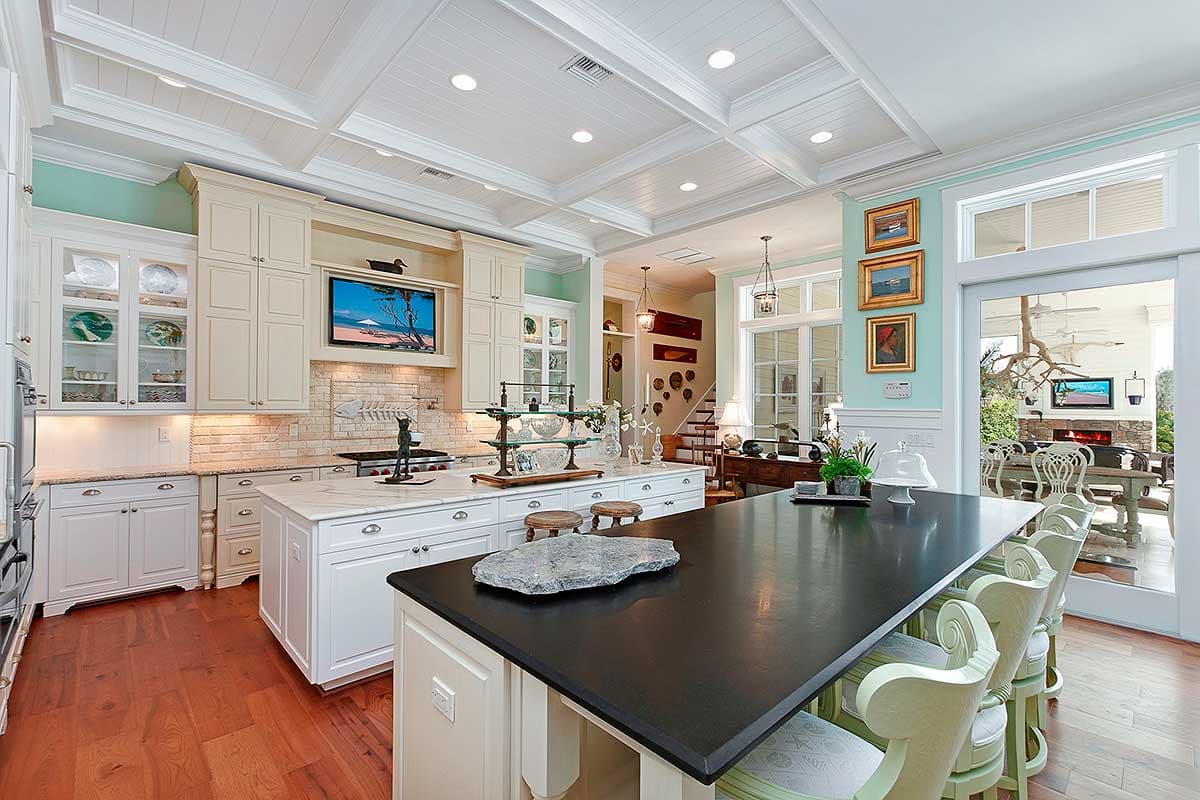 Kitchen with coffered ceiling, island with seating, and open access to dining area with fireplace.