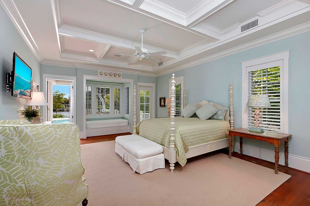 Primary bedroom with four-poster bed, bay window seat, coffered ceiling, ceiling fan, and direct patio access.