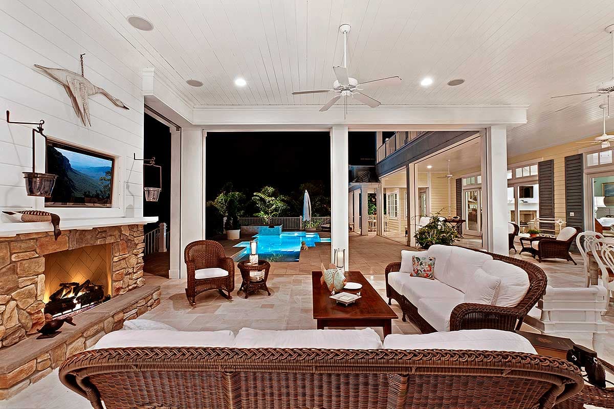 Covered patio with fireplace, seating, and view of illuminated swimming pool and house exterior.
