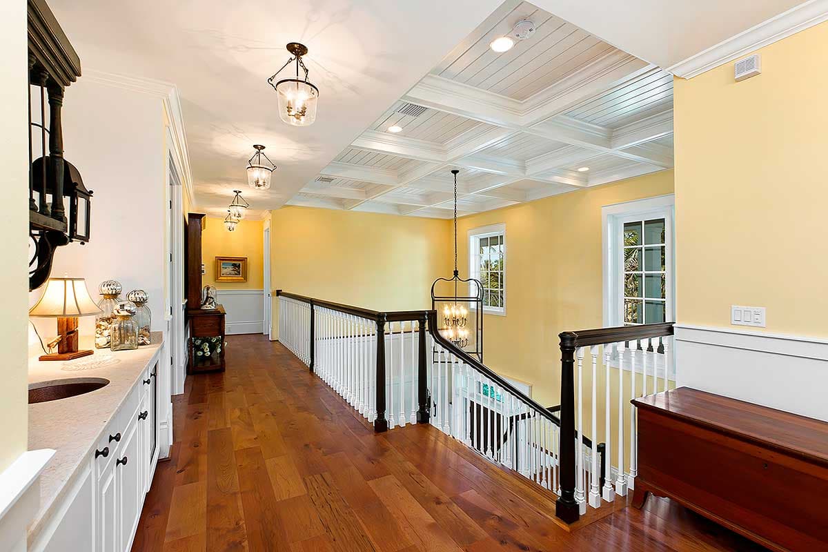 Interior view of a hallway with coffered ceiling, pendant lights, wooden floors, and a staircase with white balusters.