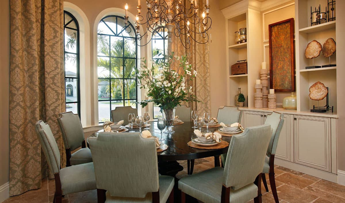 Dining room with a table set for eight, arched windows, built-in shelving with decorative items.