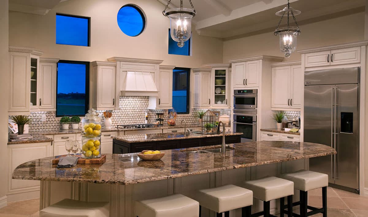 Kitchen interior with cream cabinetry, a large granite island with seating, stainless steel appliances, and distinctive blue-tinted windows.