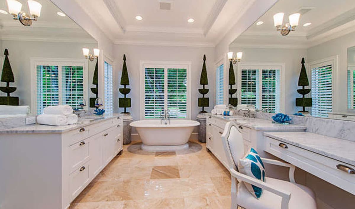 Bathroom interior with freestanding tub, double vanities, marble countertops, and coffered ceiling.