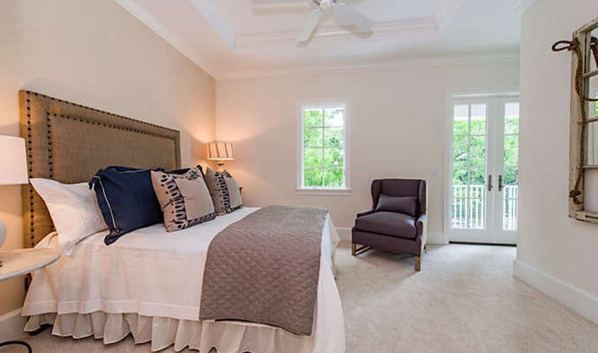 Interior view of bedroom with tufted headboard, ceiling fan, single window, and French doors leading to a balcony.