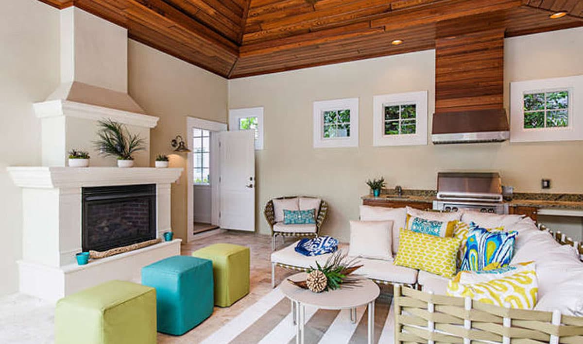 Outdoor living space with fireplace, grill, seating, and wood-paneled vaulted ceiling.