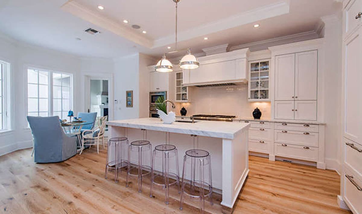 Kitchen interior with large island, seating area with chairs, cabinetry, and pendant lighting.