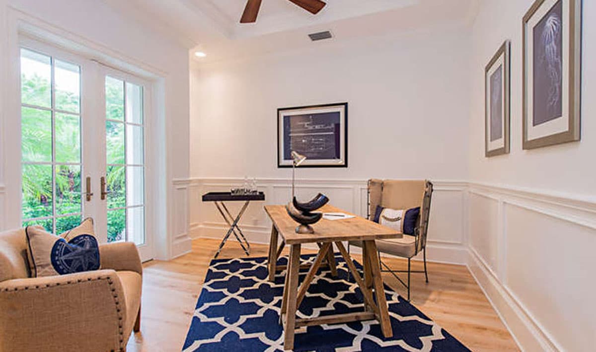 Home office with French doors, wood desk, chair, sofa, and geometric rug.