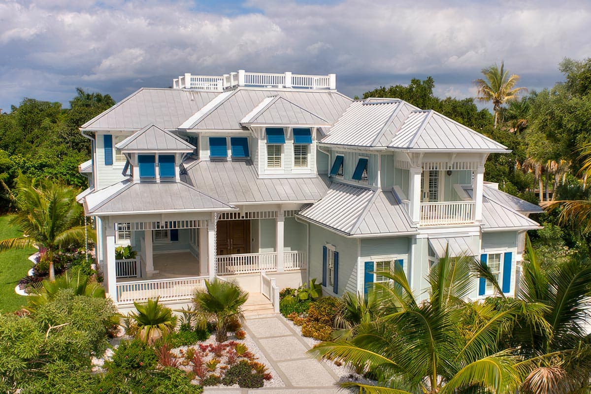 House plan exterior. Two-story coastal home with multiple gables, metal roof, covered porch, and small balconies. Blue shutters and trim.