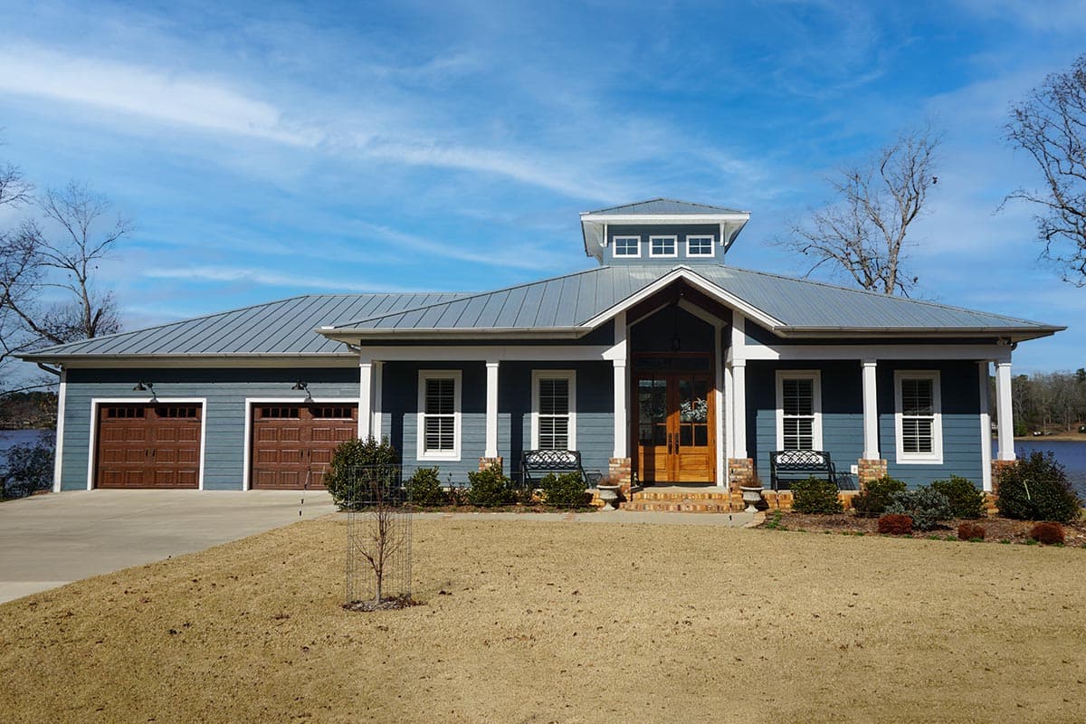 House plan exterior: One-story Modern Farmhouse with metal roof, front porch, three-car garage, and central dormer.