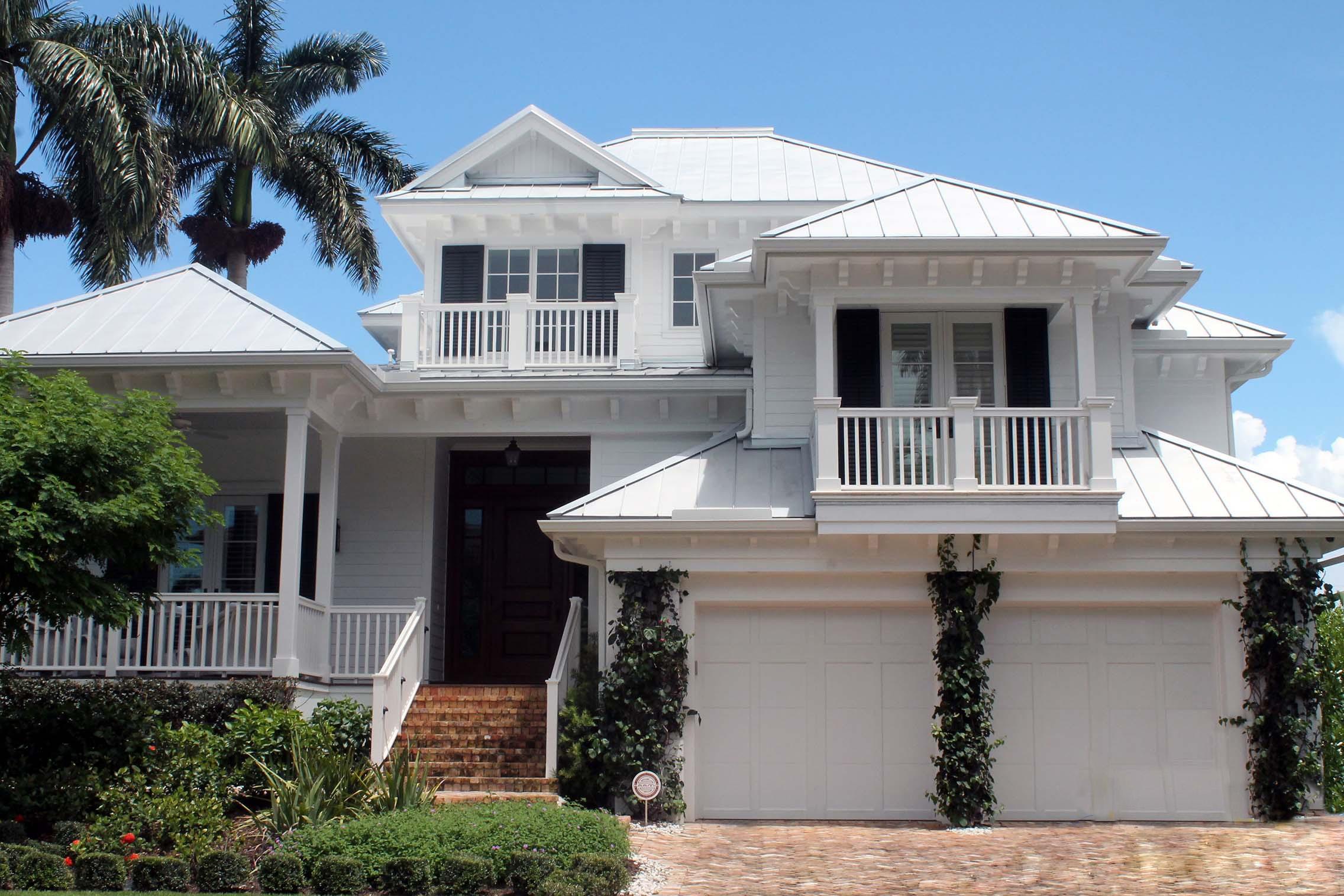 House plan exterior. Two-story, white Coastal style home with a metal roof. Features include balconies, a front porch, and a two-car garage.