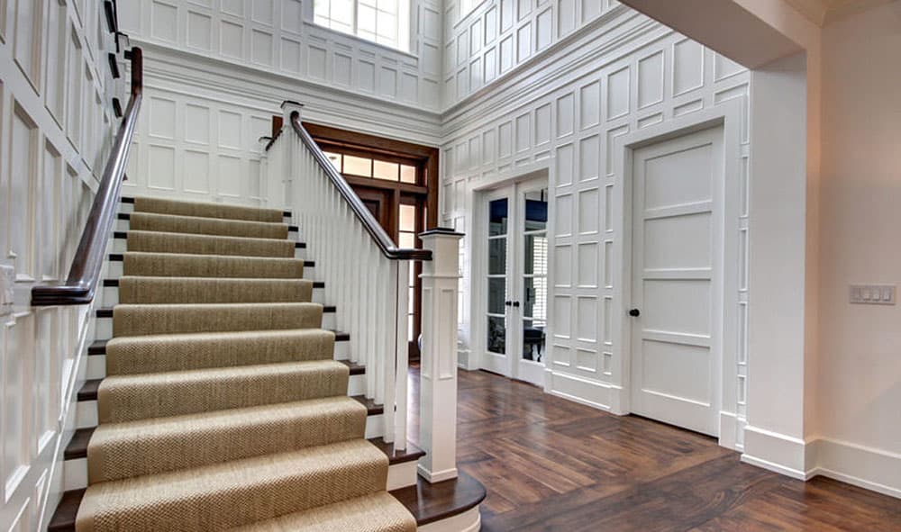 Foyer interior with paneled walls, carpeted staircase, wood flooring, and double doors.