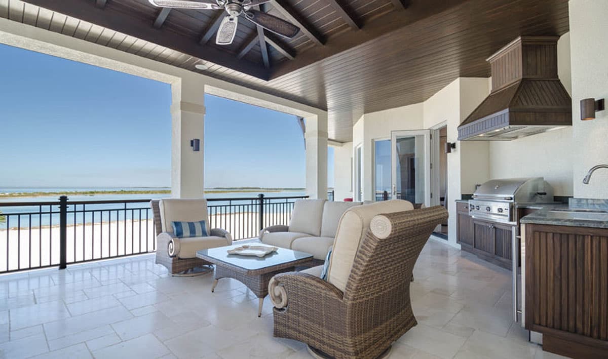 Covered outdoor living area with seating and built-in grill, overlooking water and beach.