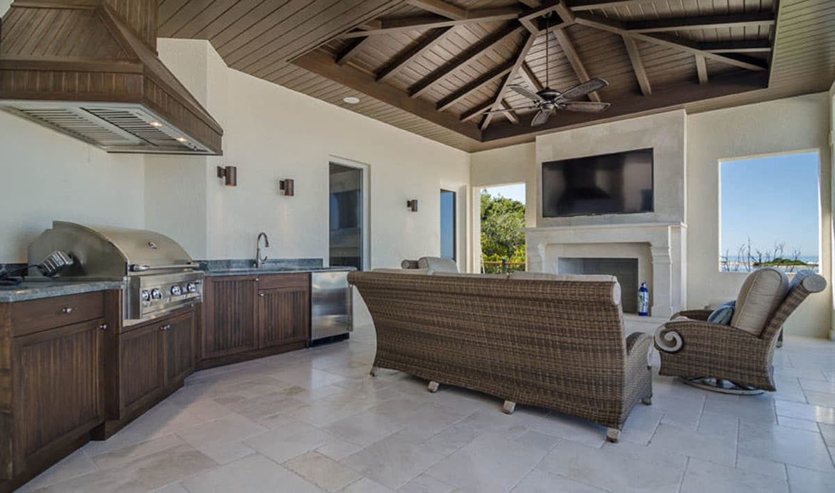 Covered outdoor living space with built-in grill, fireplace, seating, and vaulted wood-paneled ceiling.