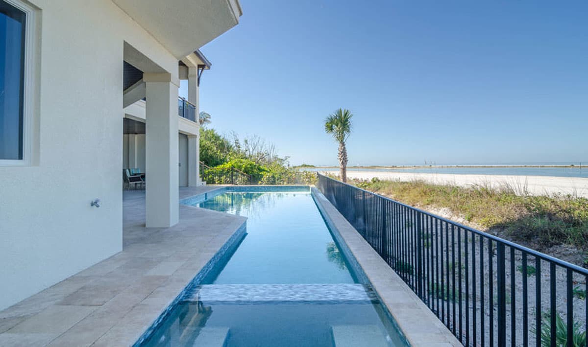 Modern house exterior with infinity pool, balconies, and ocean view.