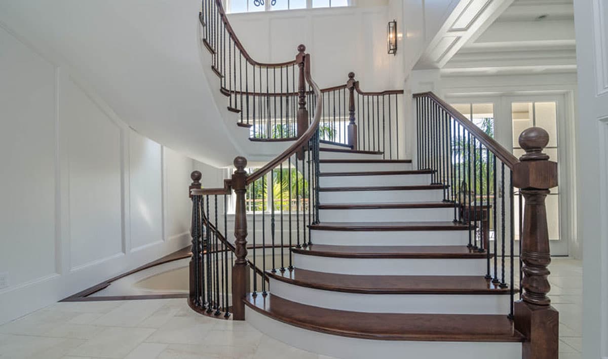 Interior view of a grand curved staircase with dark wood treads and railing, white risers, and decorative balusters.