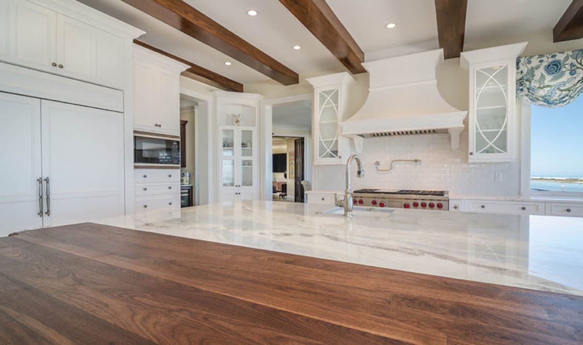 Kitchen interior with white cabinets, marble island, stainless steel range, and exposed wood ceiling beams.
