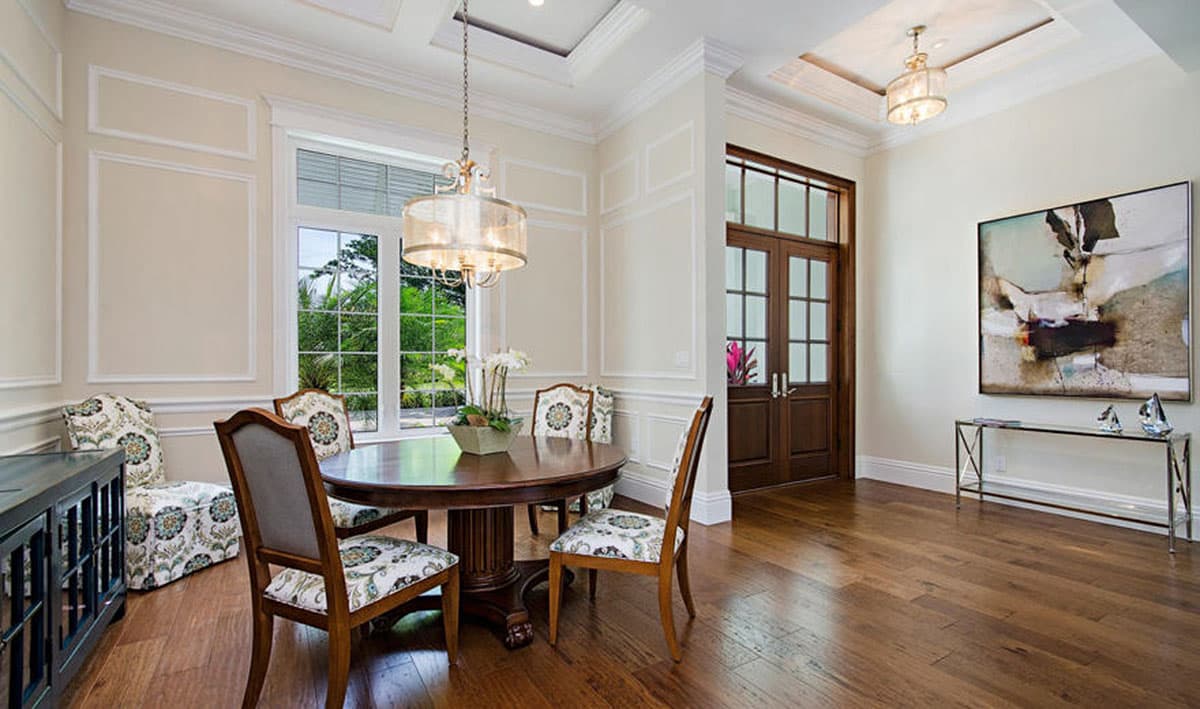 Interior view of a dining room with a round table, upholstered chairs, wainscoting, and double doors.