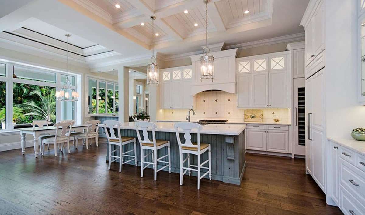 Kitchen with island, white cabinetry, coffered ceiling, and large windows overlooking tropical foliage.
