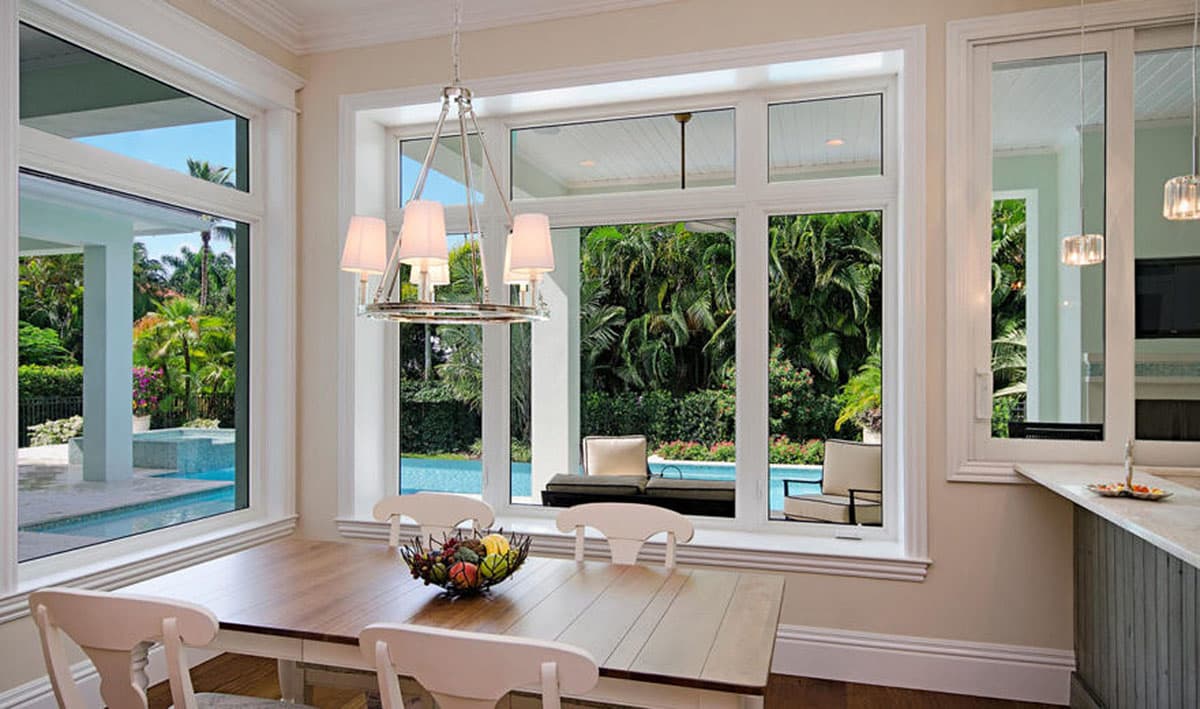 Dining area with large windows overlooking a pool and tropical landscaping. Modern chandelier hangs above.