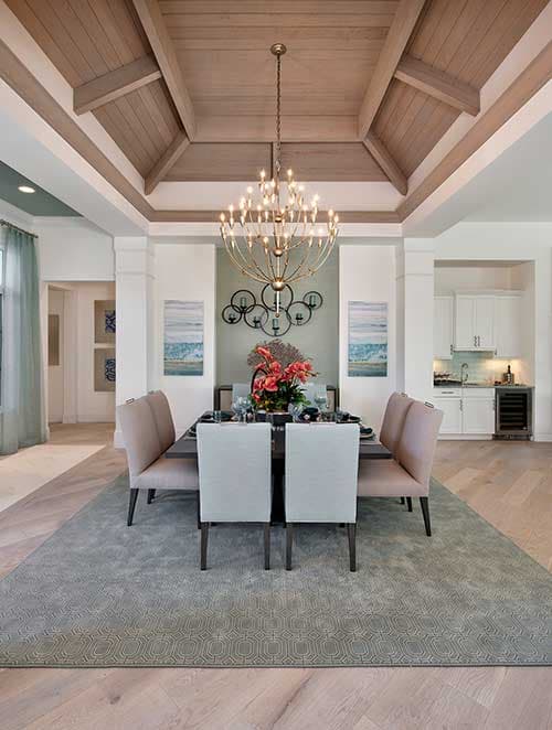 Dining room with vaulted wood-paneled ceiling, chandelier, seating for eight, and view of kitchen area.