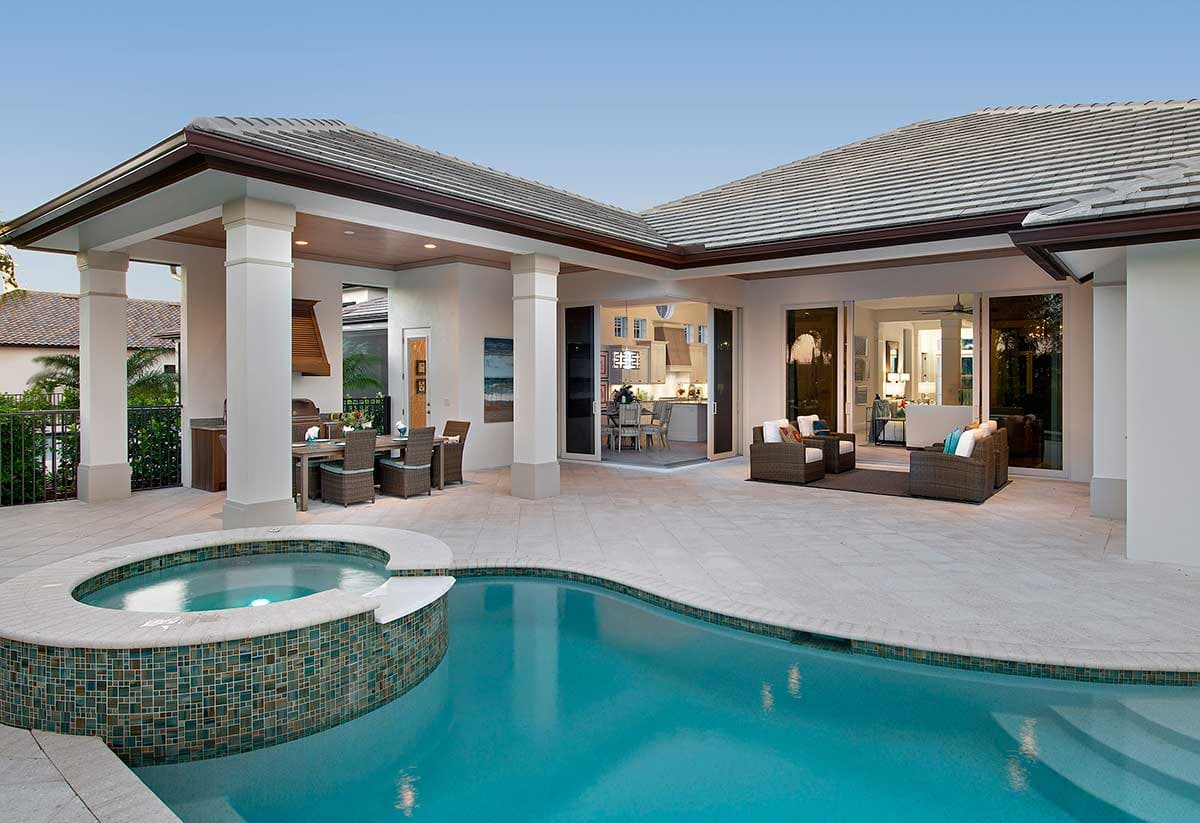 Modern home exterior with covered patio, outdoor kitchen, swimming pool, and spa. Large sliding glass doors open to interior.