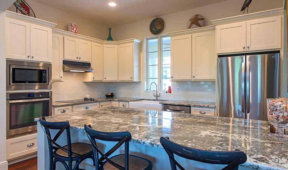 Kitchen with white cabinetry, stainless steel appliances including double ovens and refrigerator, and a large granite island.