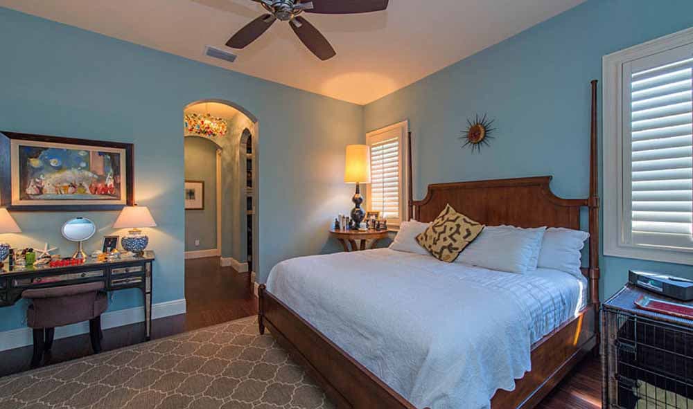 Bedroom with wood bed, desk, arched doorway to hallway, and plantation shutters.