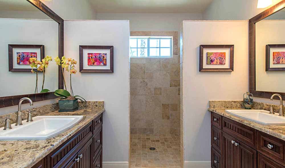 Bathroom with dual vanities, granite countertops, dark wood cabinets, and a walk-in shower with tiled walls.