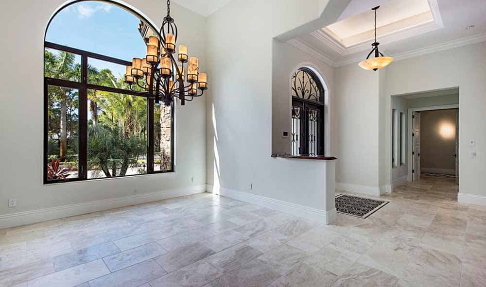 Interior view of a large room with a high, arched window, ornate chandelier, and marble tile flooring.