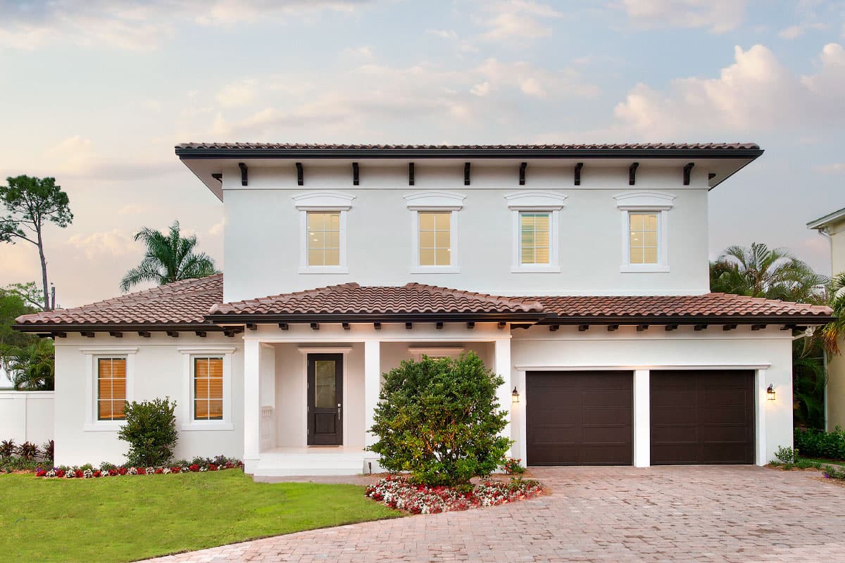House plan exterior. Two-story Mediterranean-style home with tile roof, covered porch, and two-car garage. Features decorative window trim.