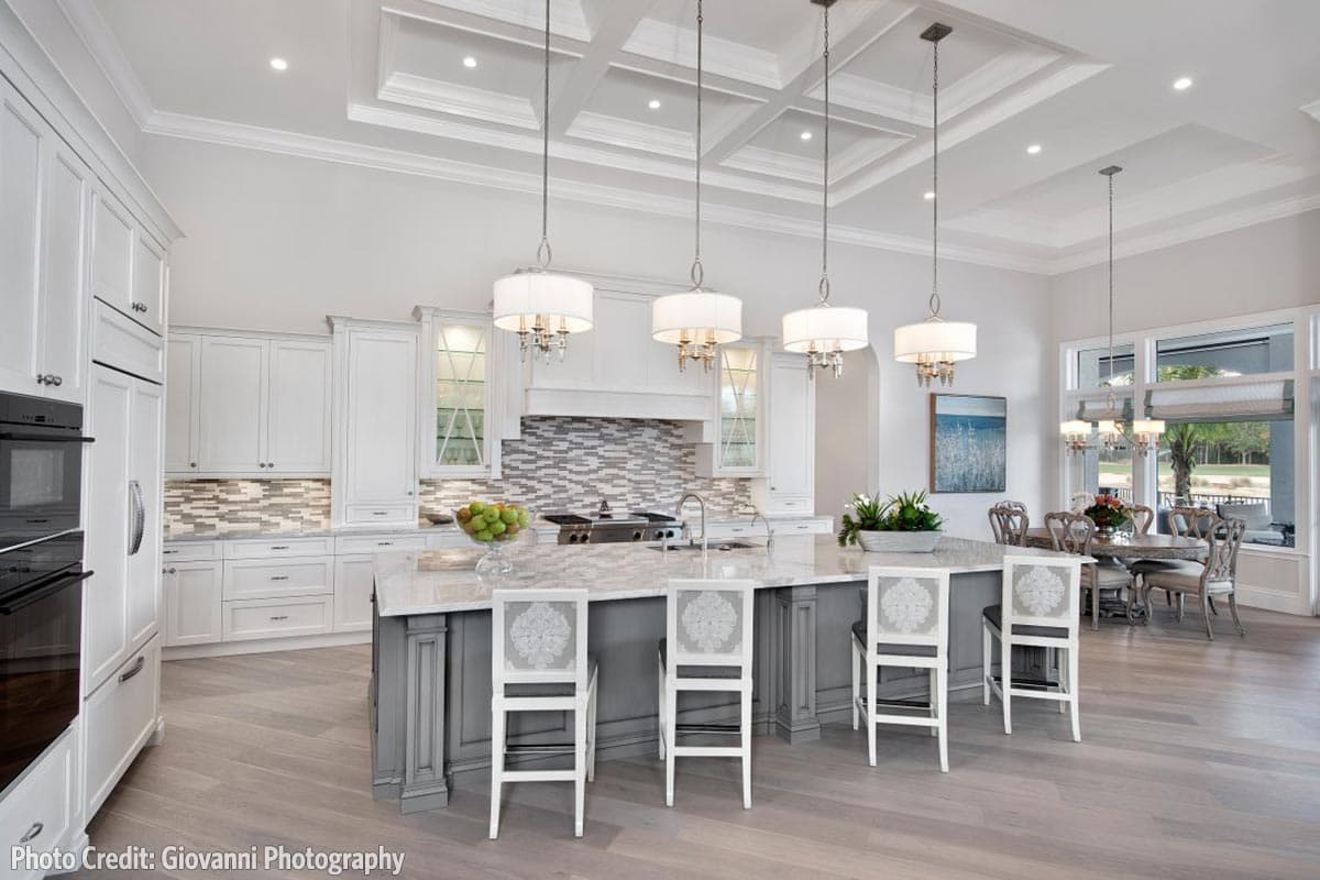 Kitchen with coffered ceiling, island with bar seating, white cabinetry, mosaic tile backsplash, and adjacent dining area.