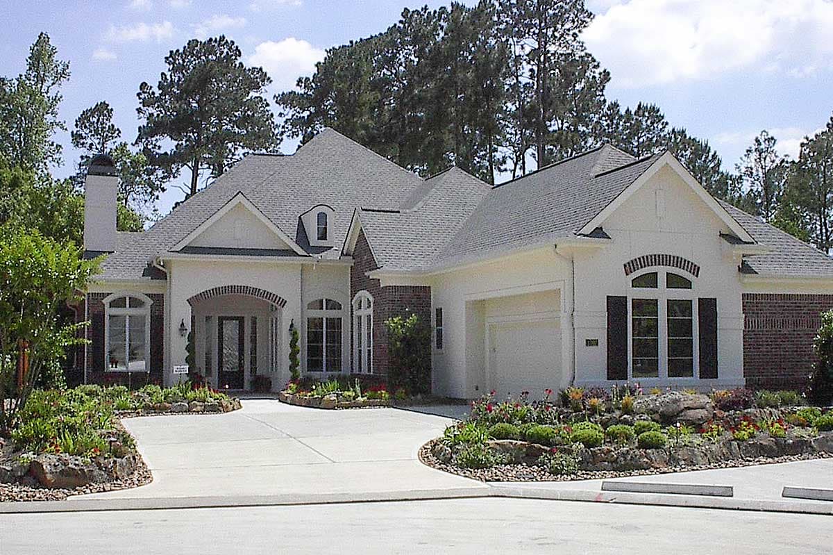 House plan exterior with brick accents, arched window, and attached garage. Features multiple gables and dormer window.