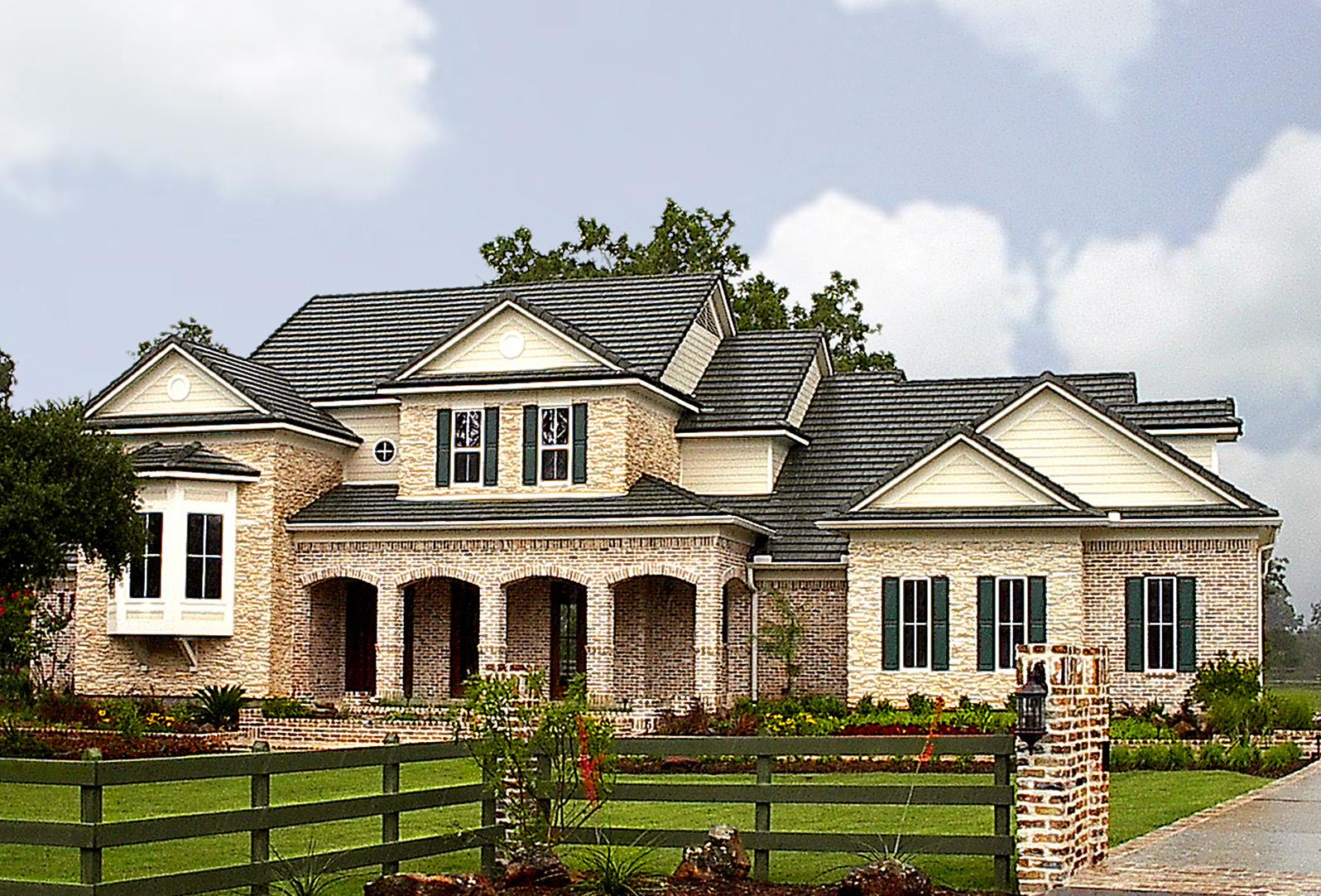 House plan exterior featuring a two-story brick and stone facade, arched entryway, bay window, multiple gables, and dark shingle roof.