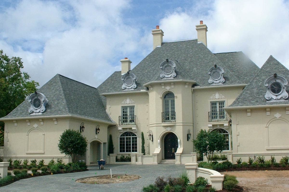 House plan exterior featuring Mansard roof, dormers with decorative louvers, arched doorways, and Juliet balconies.