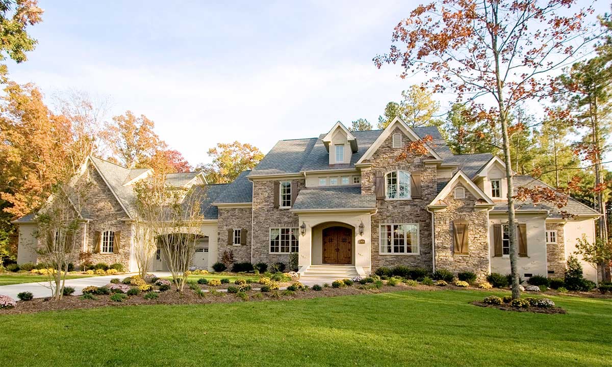 House plan exterior. Two-story home with stone facade, multiple gables, arched entry, dormers, and attached garage with side entry.