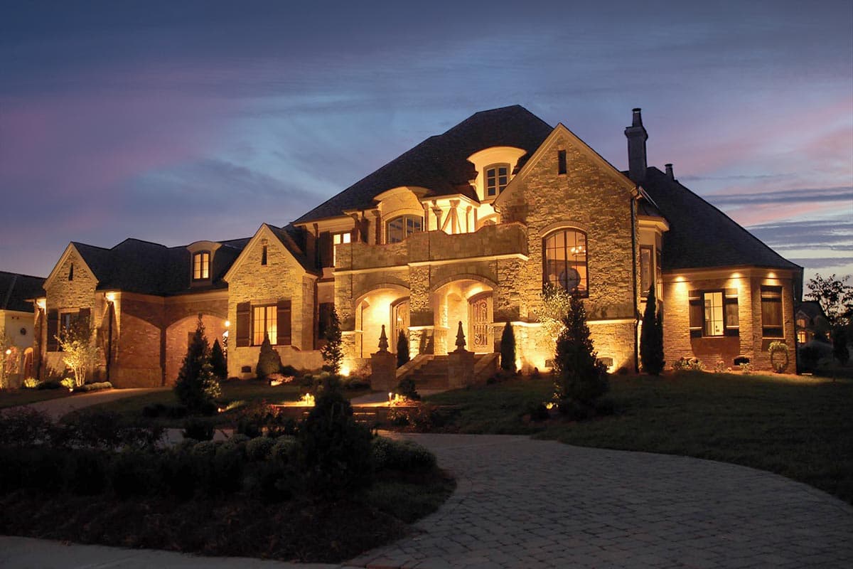House plan exterior of a two-story stone and brick home with gabled dormers, arched entryways, and a curved driveway.