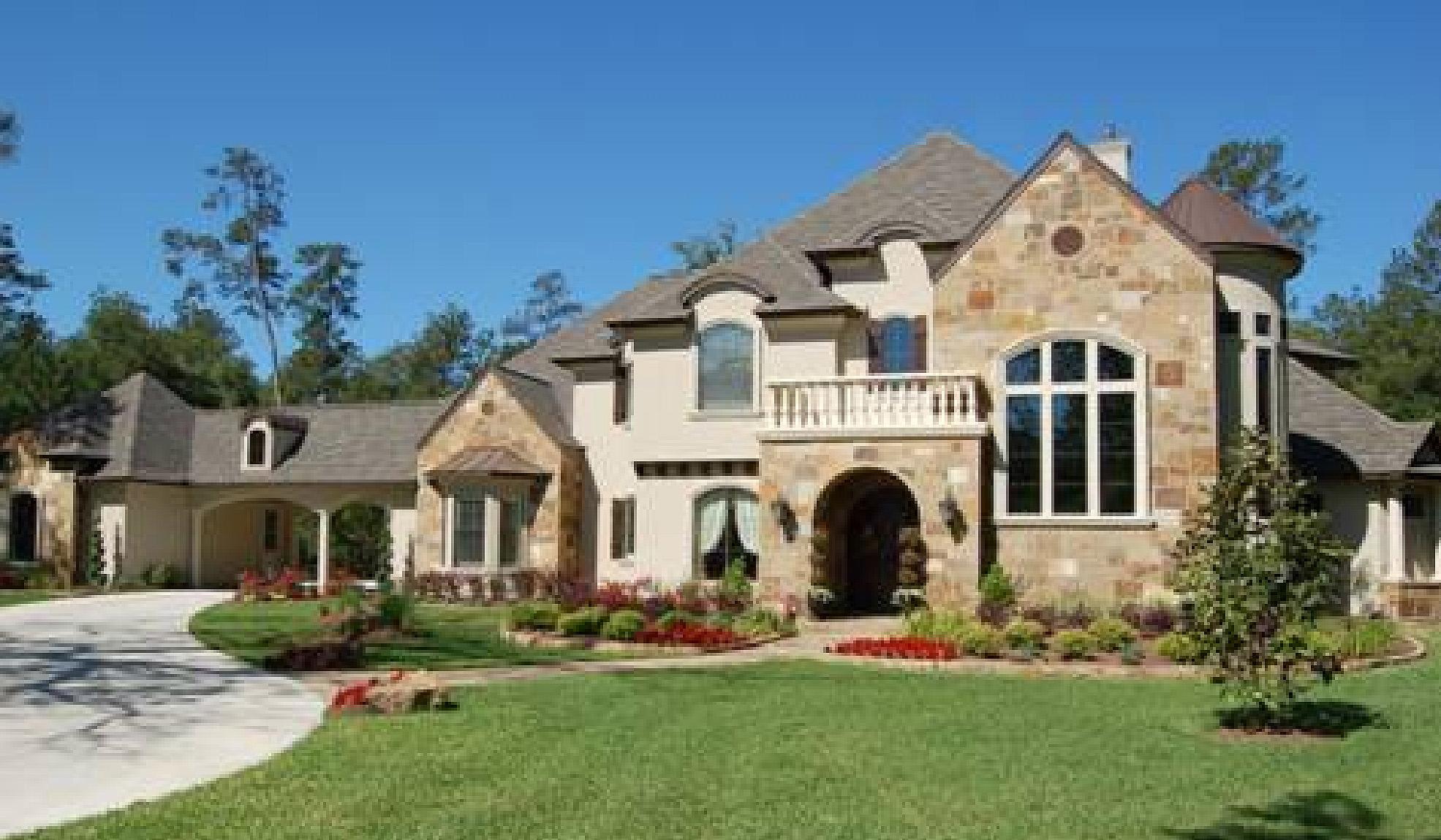 House plan exterior: Two-story home with stone accents, arched entryway, balcony, and a detached three-car garage.