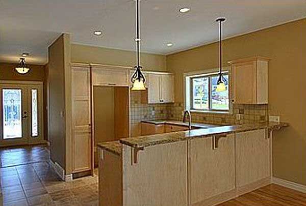 Interior view of a kitchen with light wood cabinets, granite countertops, a peninsula, and double entry doors visible in the hallway.