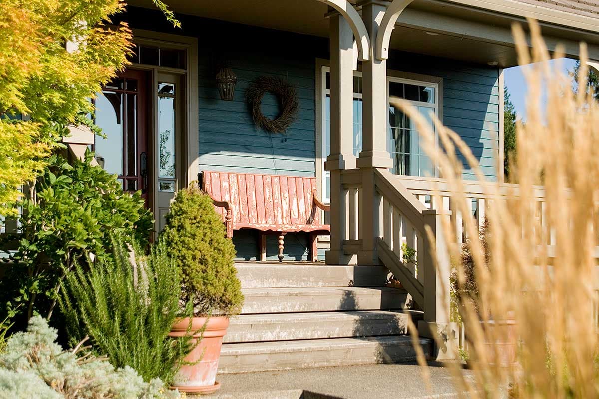Craftsman style house plan exterior with a covered porch, wood siding, double-hung windows, and a decorative bench.